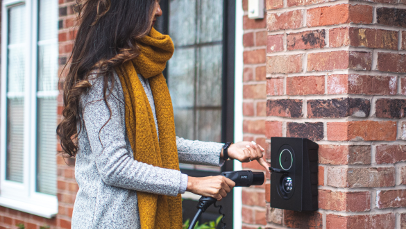 Eine Frau steht an einer Wallbox und hält das Ladekabel für ihr Elektroauto in der Hand