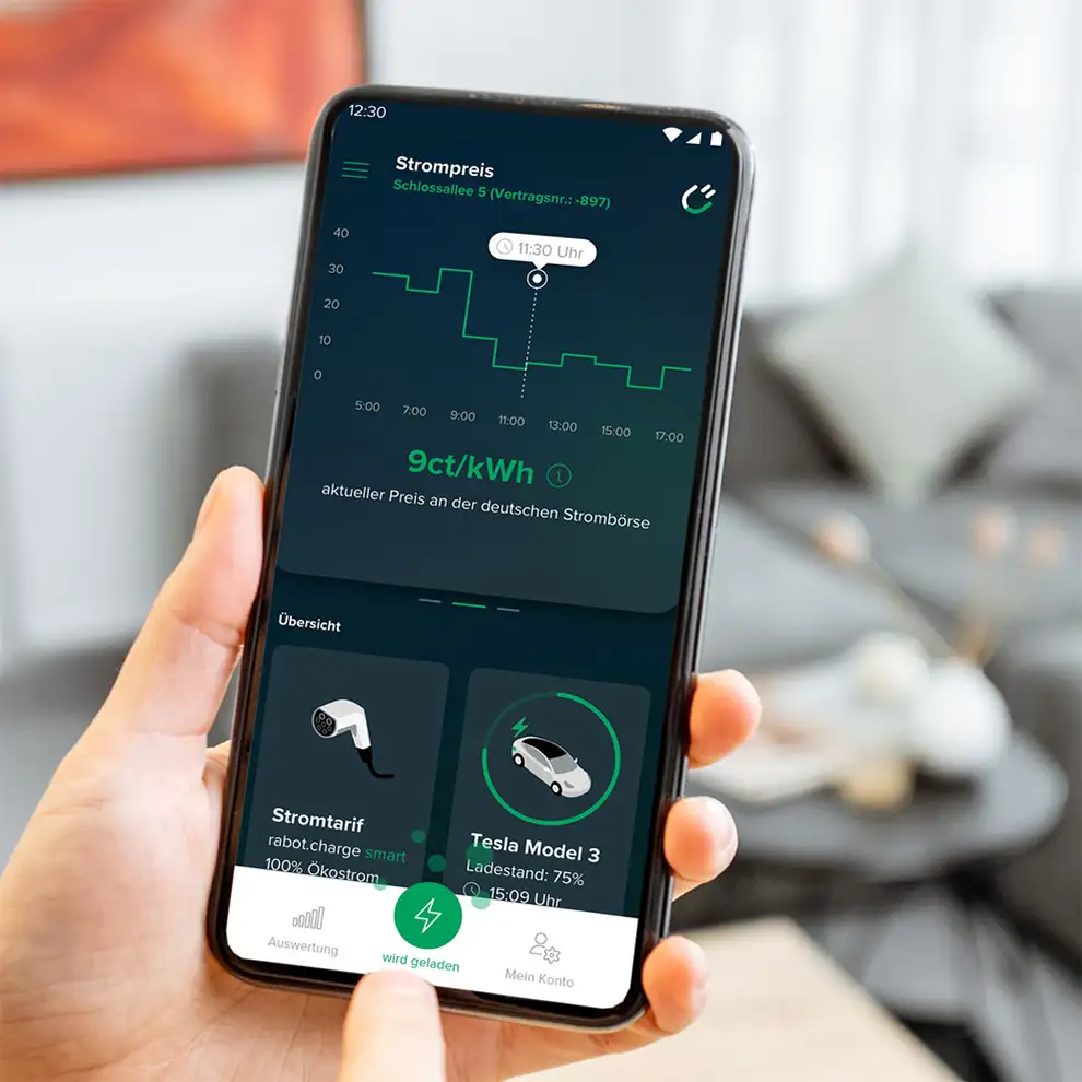 Eine Hand hält ein Smartphone, das die Strompreisübersicht einer Energiemanagement-App anzeigt. Der aktuelle Preis liegt bei 9 ct/kWh. Ein Diagramm zeigt die Preisentwicklung über den Tag hinweg. Weitere Informationen auf dem Bildschirm beinhalten den Stromtarif und den Ladestand eines Tesla Model 3 mit 75 %. Im Hintergrund ist ein unscharfes Wohnzimmer zu sehen.